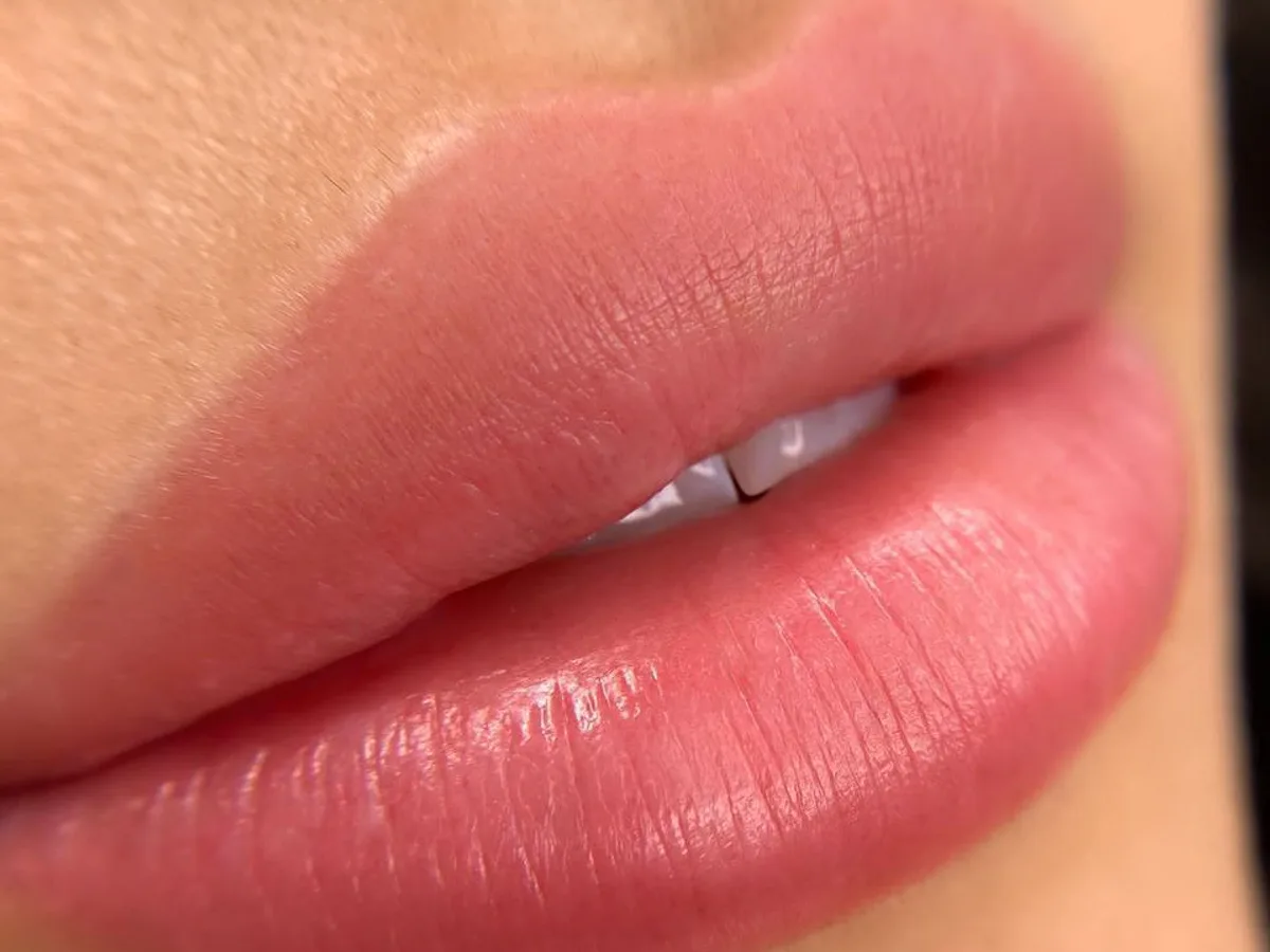 Extreme close-up of glossy, evenly toned lips showing a soft semi-permanent lip blush tint