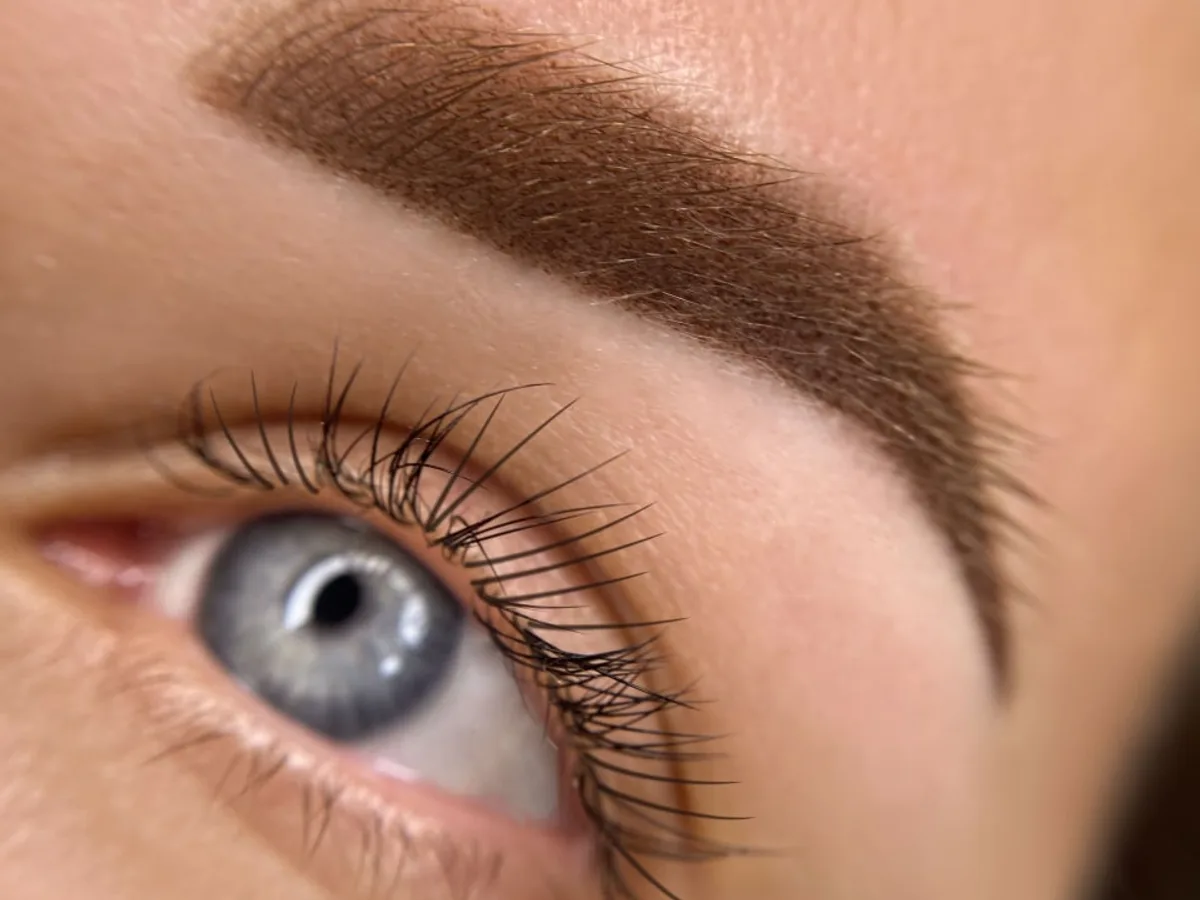 Extreme close-up of a perfectly groomed gold-lit ombre powder brow, editorial beauty photography